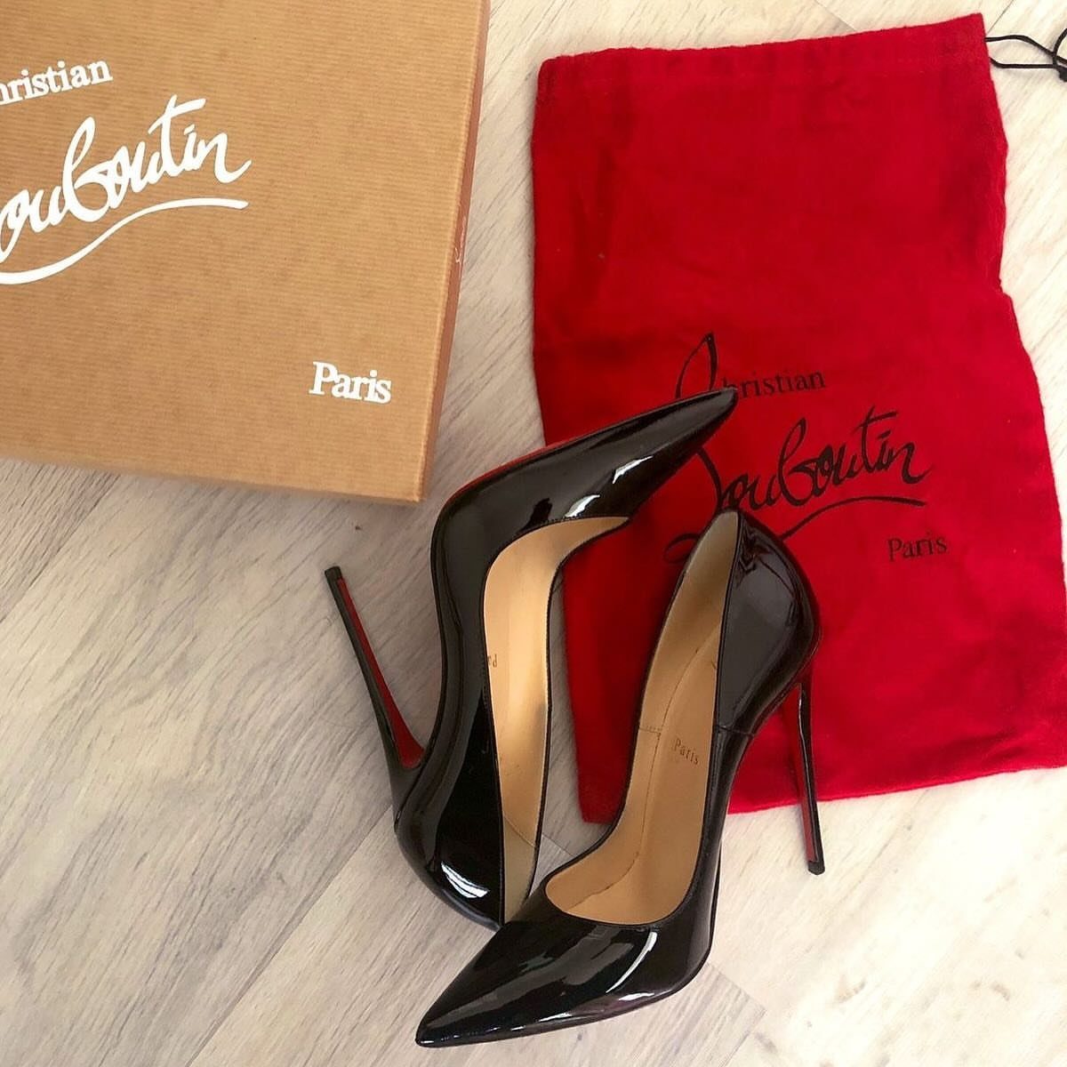 Black patent leather stiletto high heels next to a designer shoebox and red dust bag.