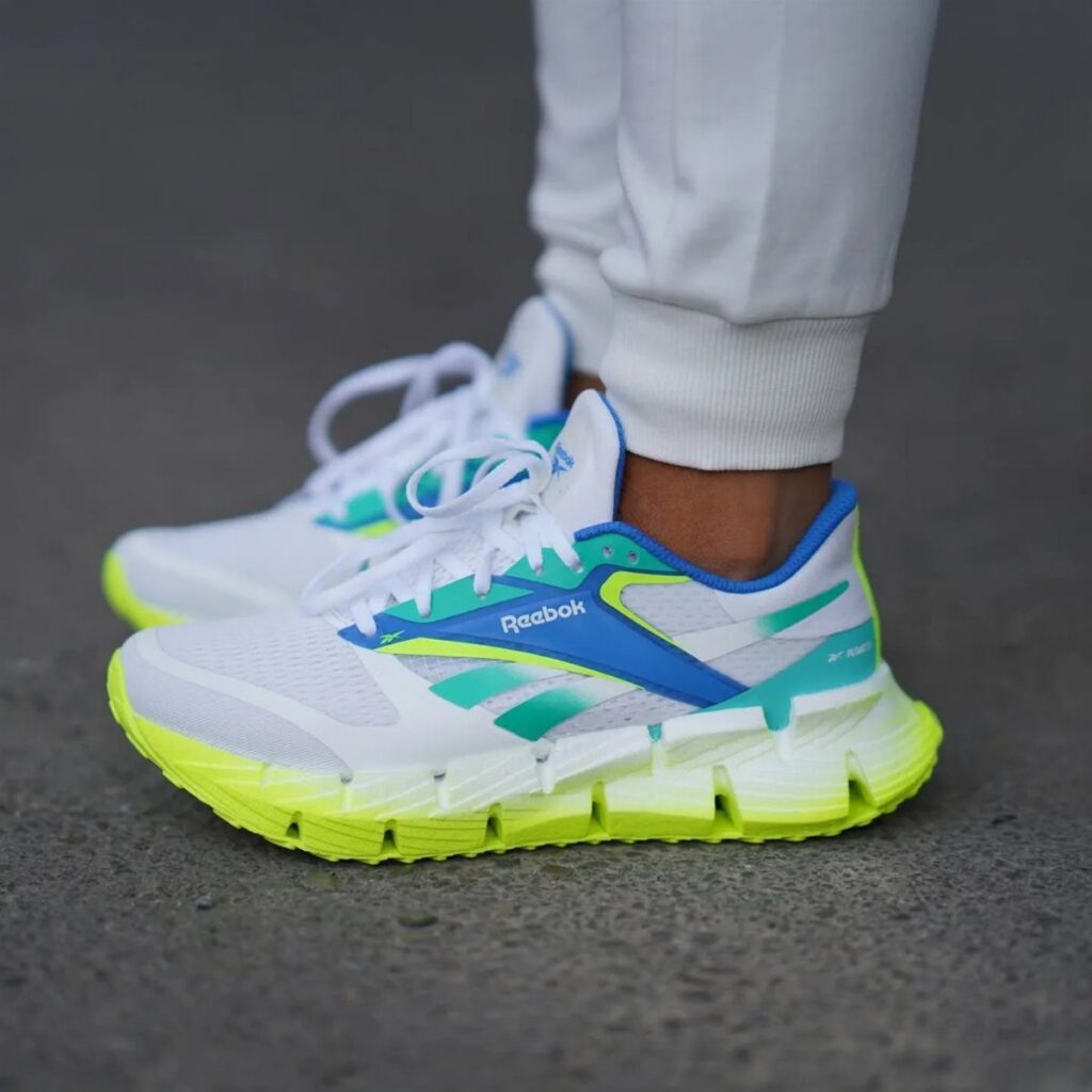 White and lime green Reebok running shoes worn by a person on asphalt.