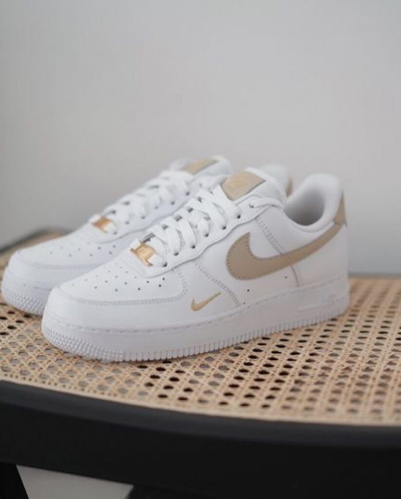 White Nike Air Force 1 sneakers with beige swooshes sitting on a woven cane stool.