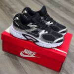 Black and silver sneakers resting on a red Nike shoebox on a wooden floor.