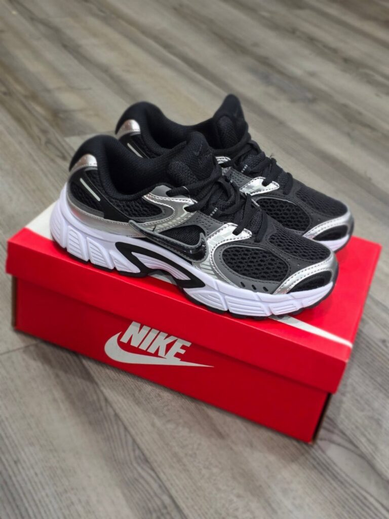 Black and silver sneakers resting on a red Nike shoebox on a wooden floor.