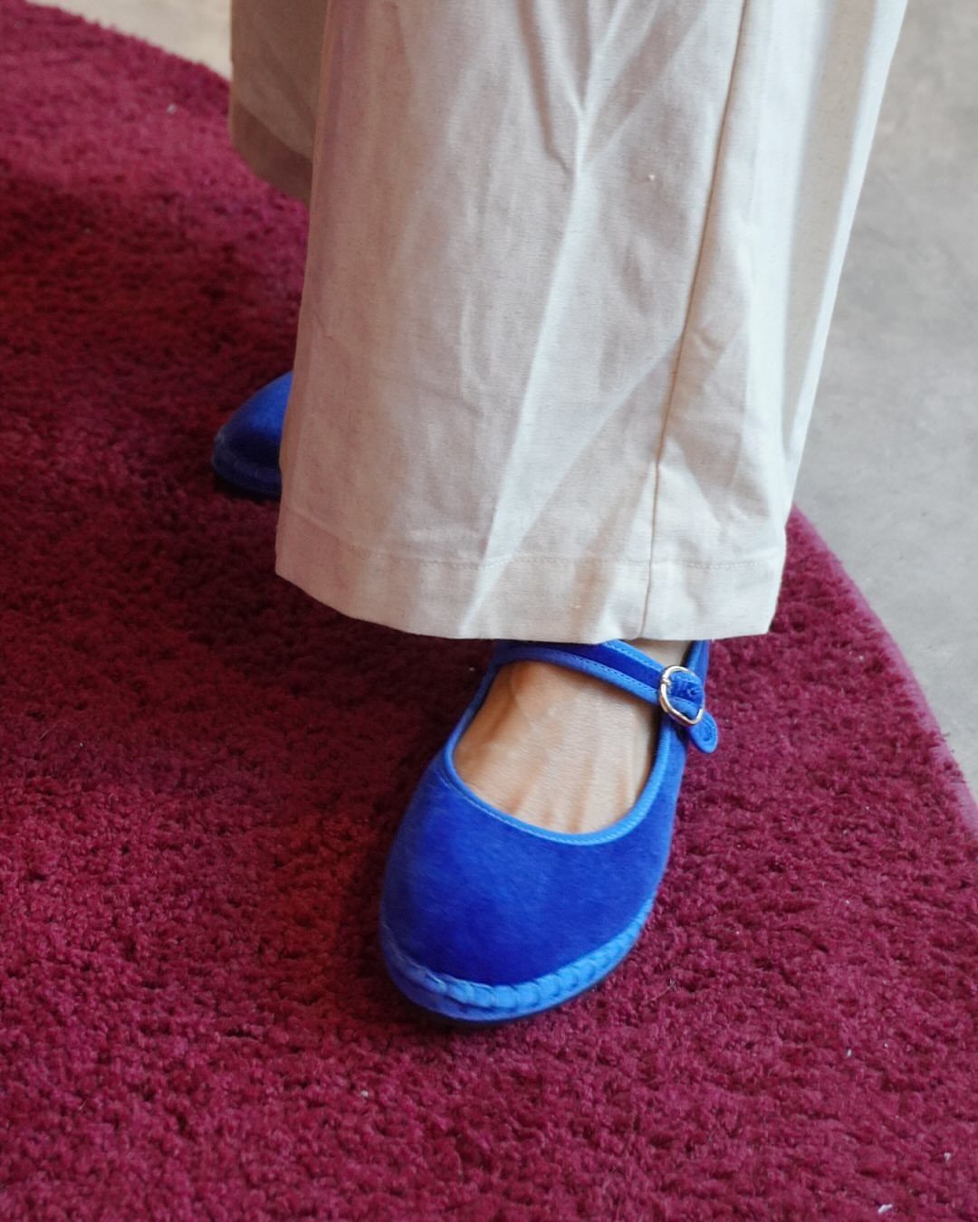 Blue velvet Mary Jane shoes worn with cream trousers on a red carpet.