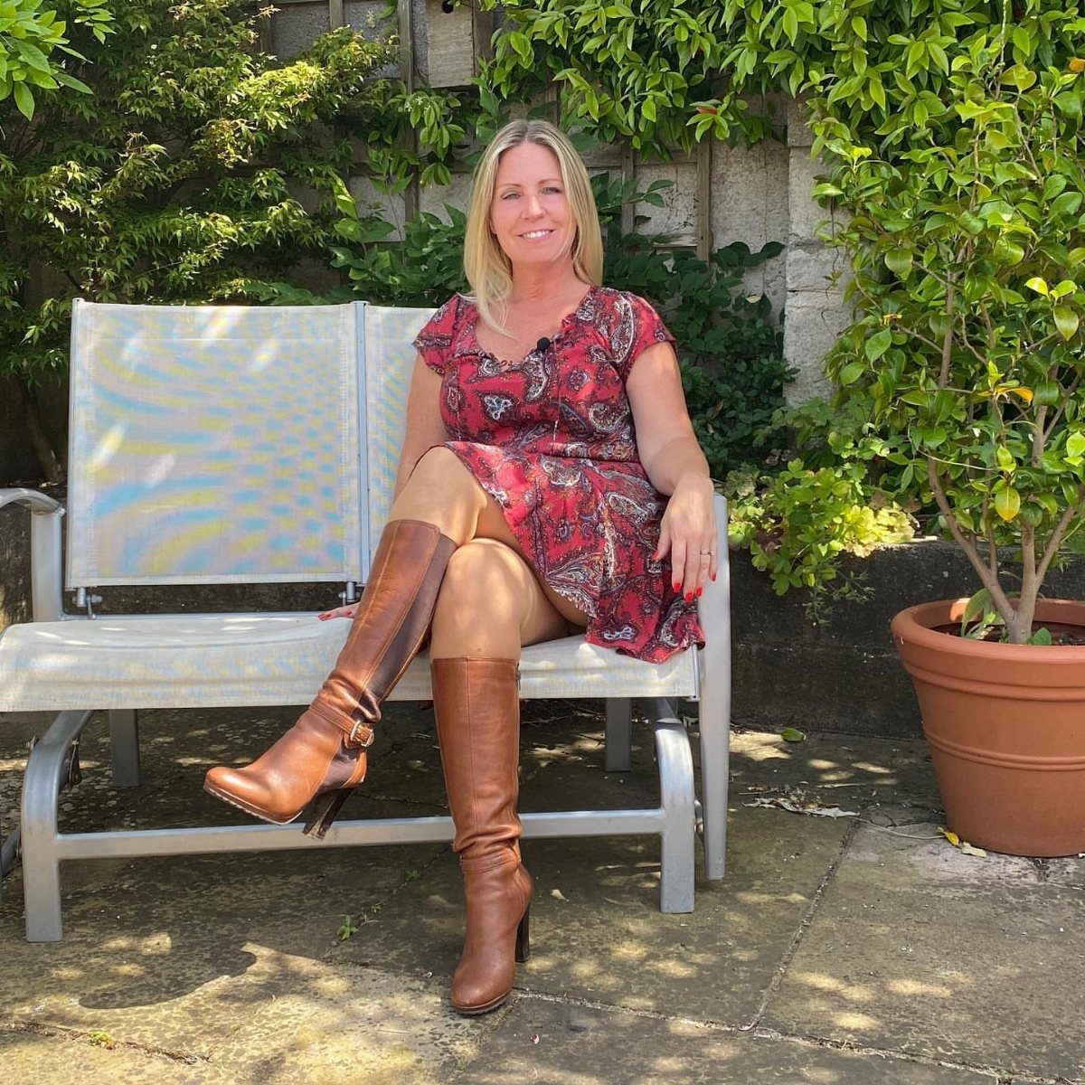 Woman in a red dress sitting on a garden chair wearing tall brown leather boots.