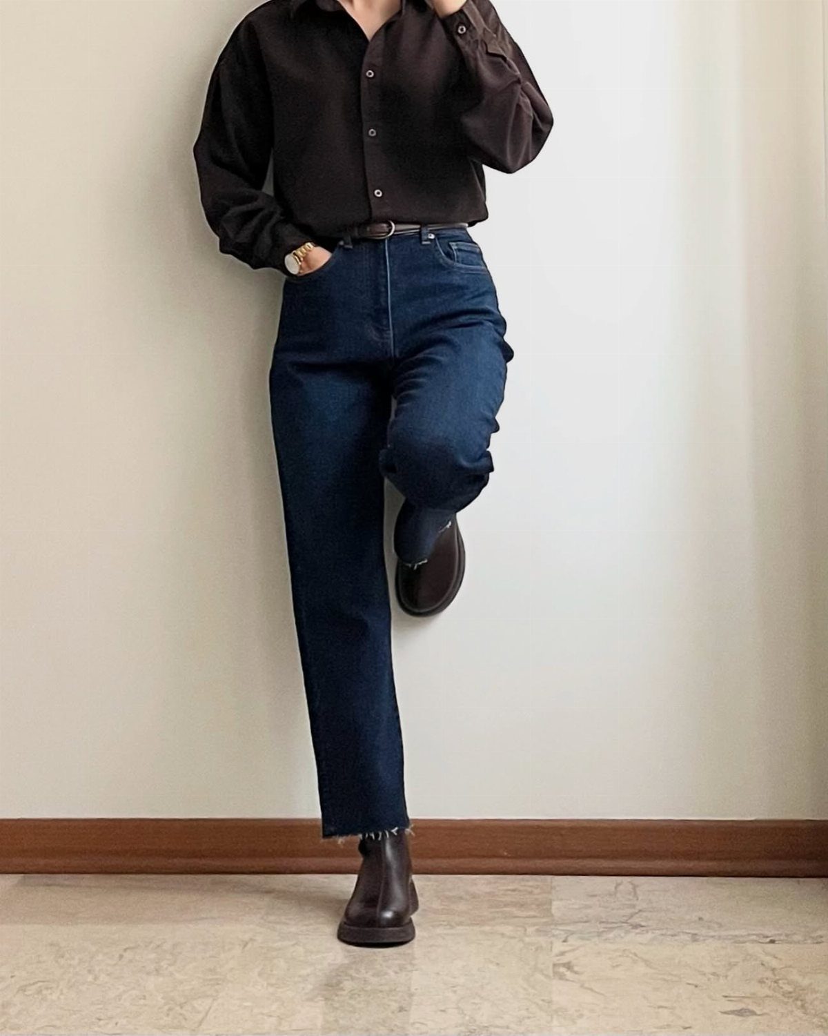A person wearing dark blue straight-leg jeans and brown Chelsea boots against a white wall.