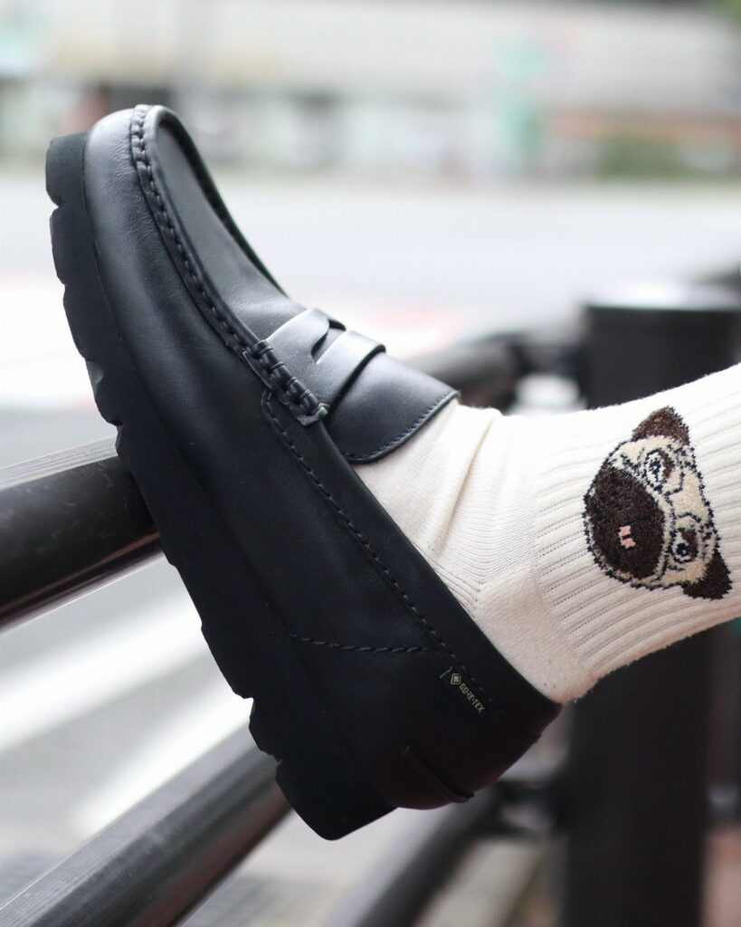 A black leather slip-on loafer worn with a pug patterned white sock on a metal railing.