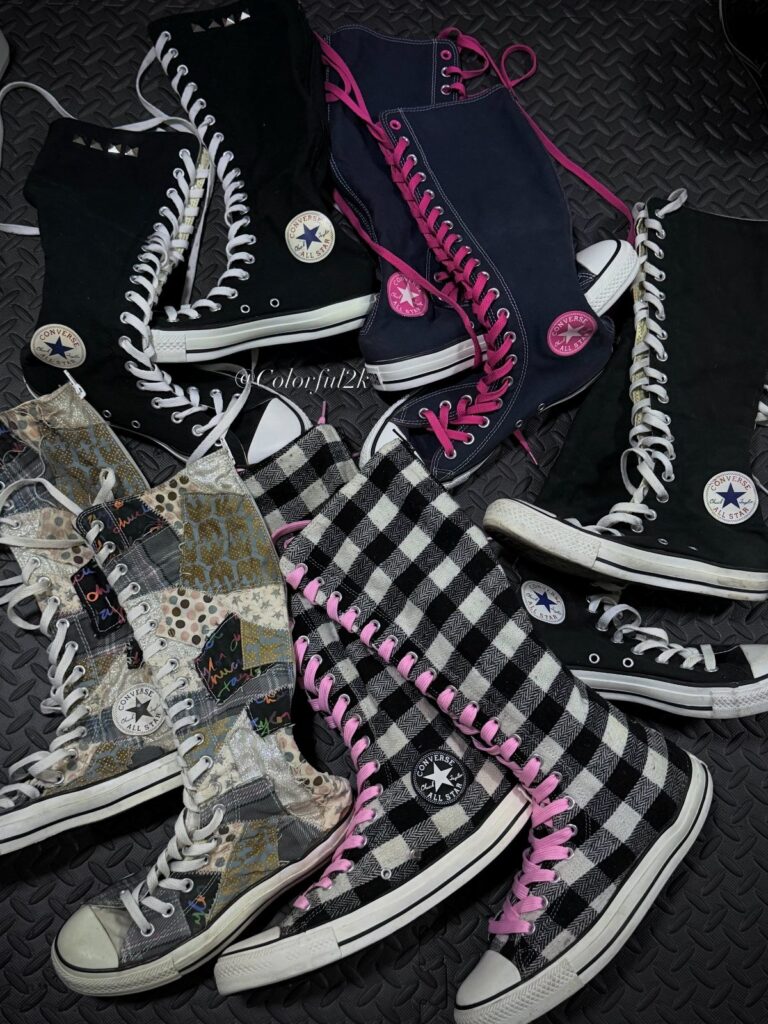 Multiple pairs of patterned and colored high-top Converse sneakers scattered on a dark surface.