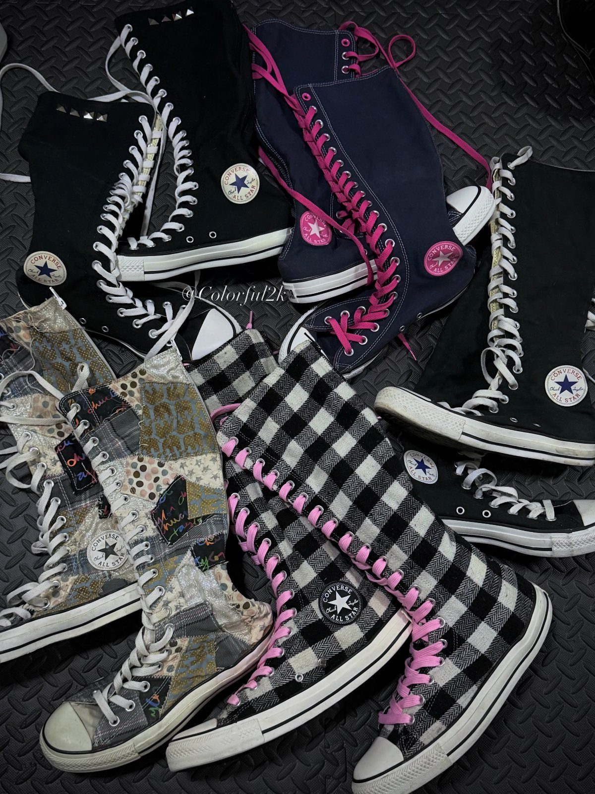 Multiple pairs of patterned and colored high-top Converse sneakers scattered on a dark surface.