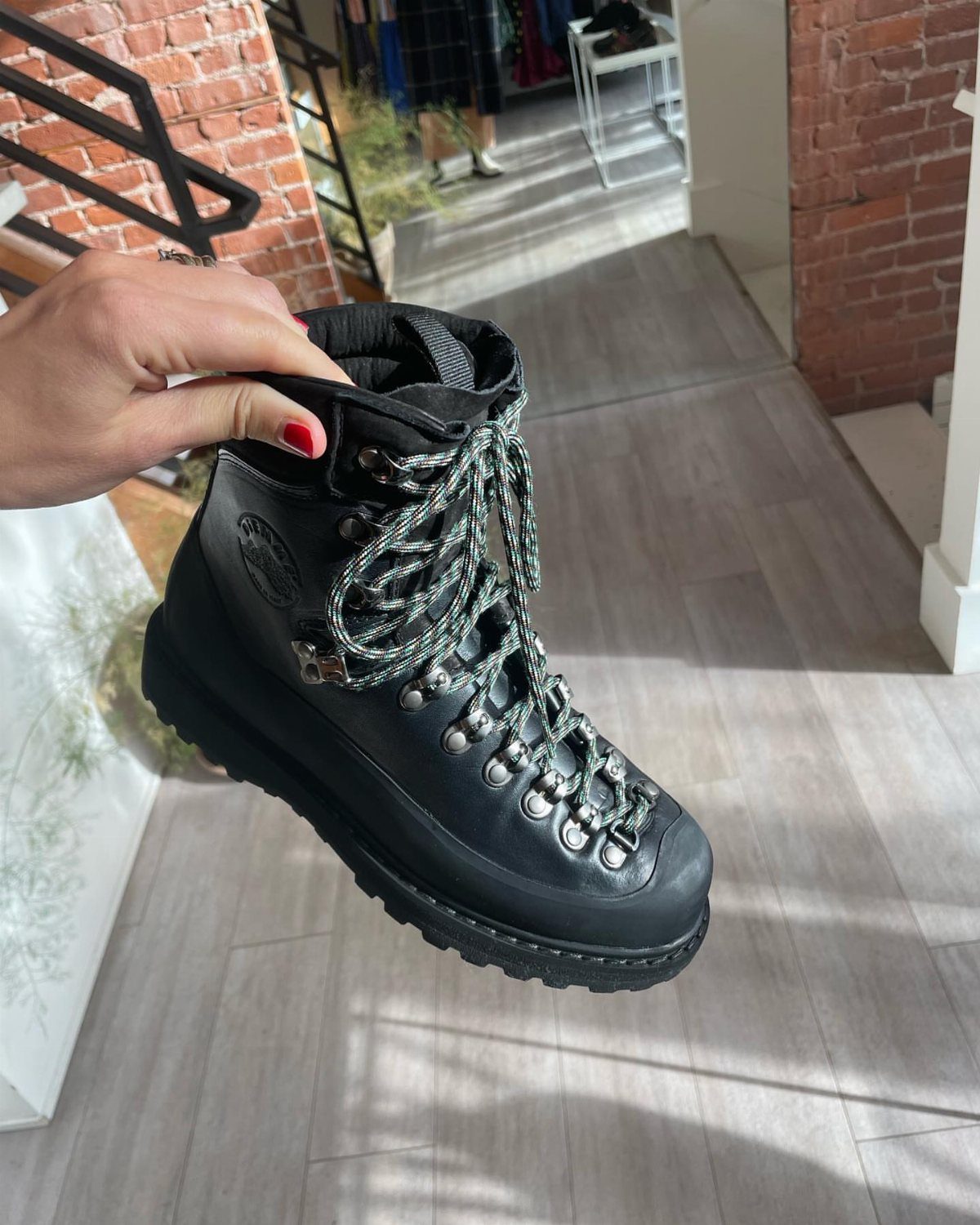 A hand holding a black leather Diemme Roccia Vet boot with patterned laces against a bright background.