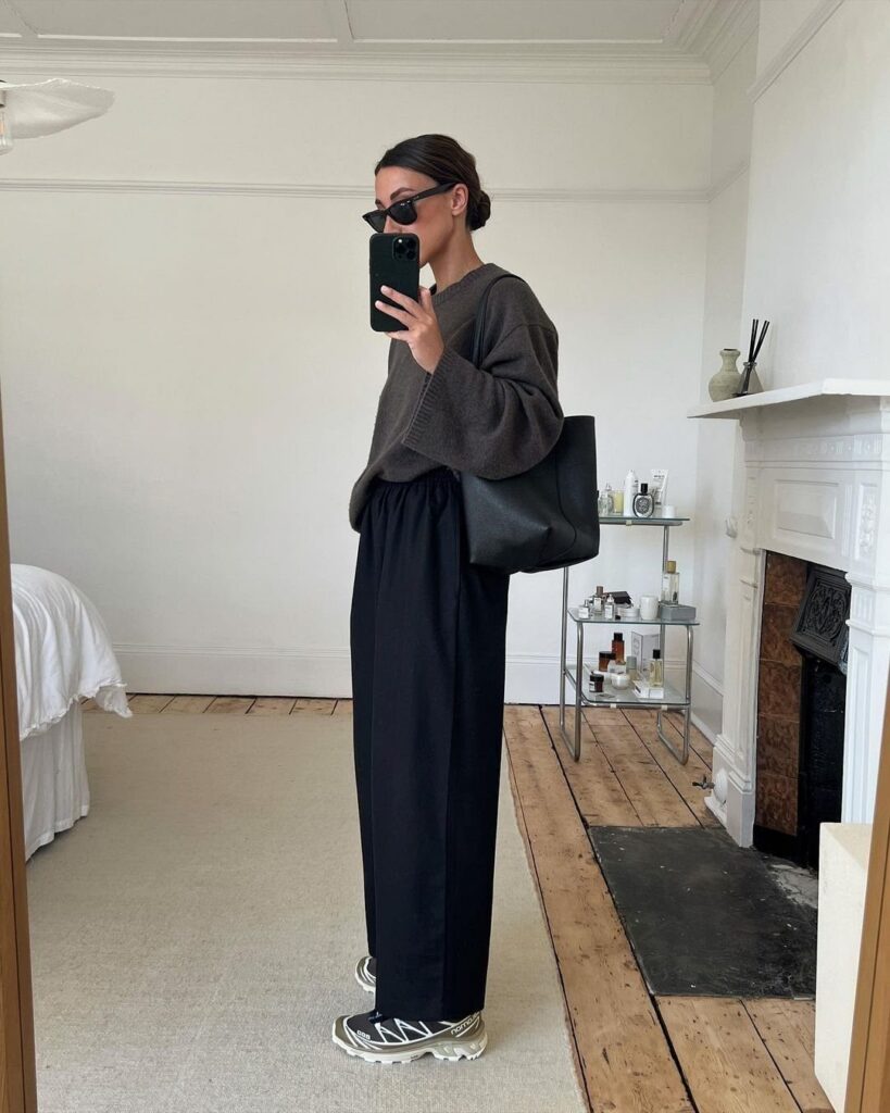 Woman in oversized sweater and wide-leg black trousers wearing silver and black sneakers.