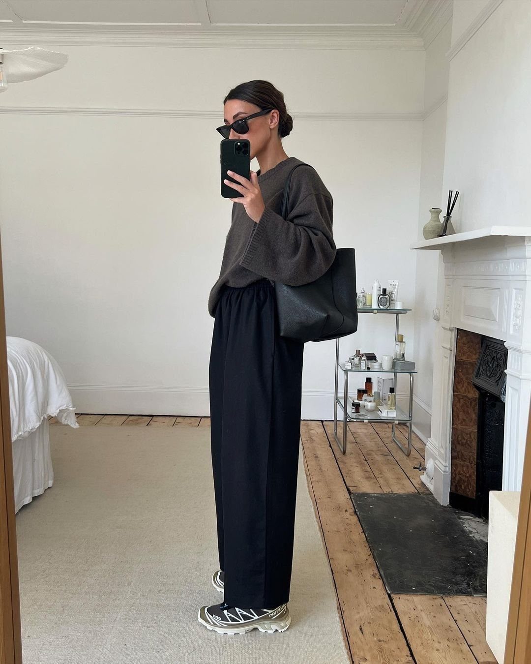 Woman in oversized sweater and wide-leg black trousers wearing silver and black sneakers.