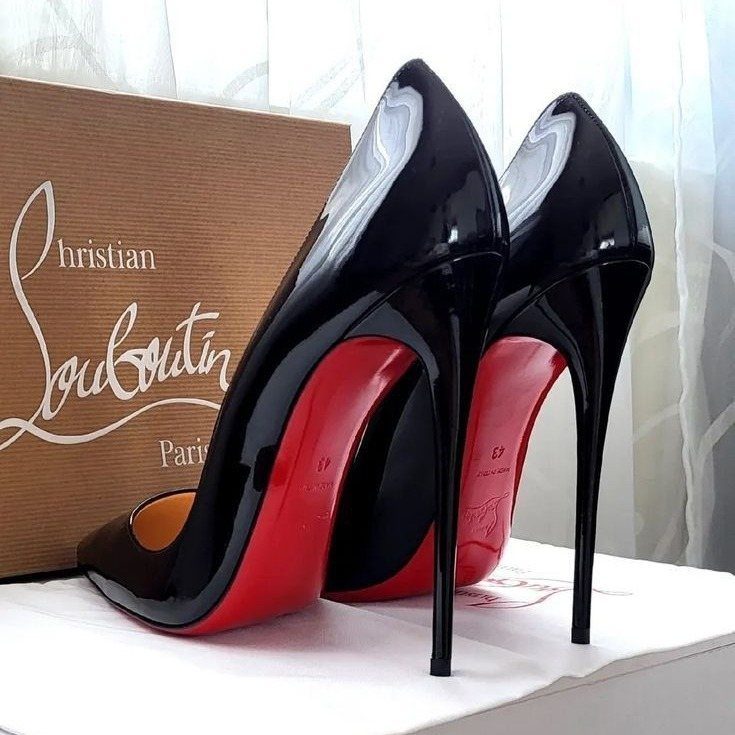 Black patent leather high heels with signature red soles resting next to a branded shoe box.