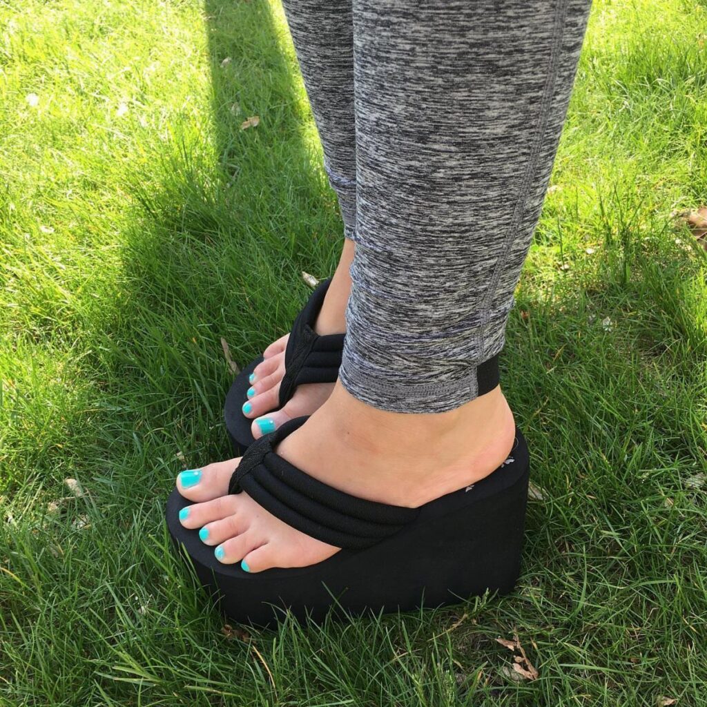 Person wearing black platform flip flops and grey leggings standing on green grass.