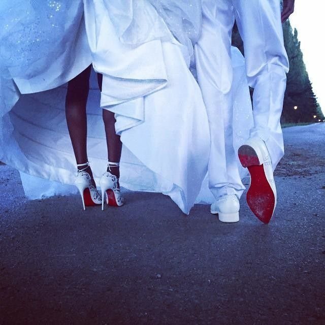Bride wearing white lace stiletto sandals with red soles standing next to a groom.
