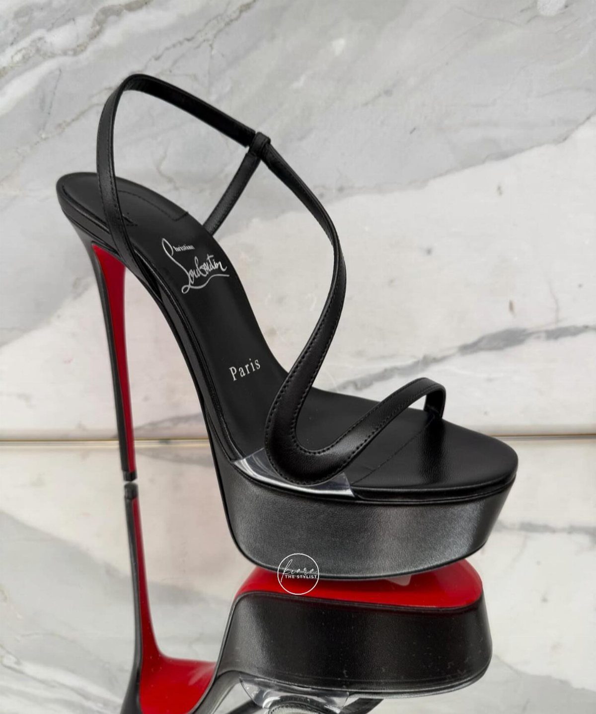 Black high-heeled platform sandal with a distinctive bright red sole on marble.
