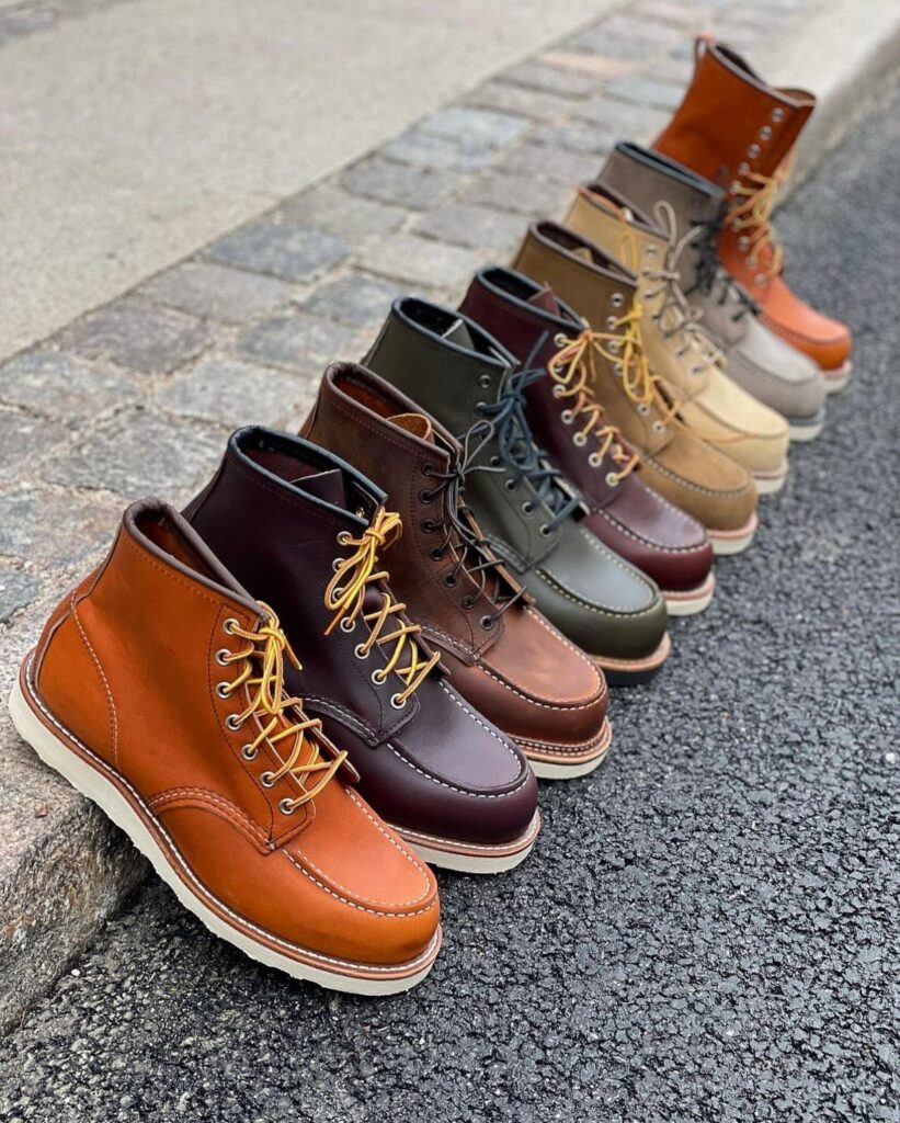 A row of leather heritage boots in various colors lined up on a paved ground.