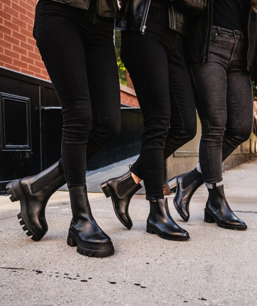 Three people walking on a sidewalk wearing black skinny jeans and various black leather boots.