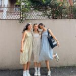 Three women posing in patterned midi dresses and white sneakers against a wall.