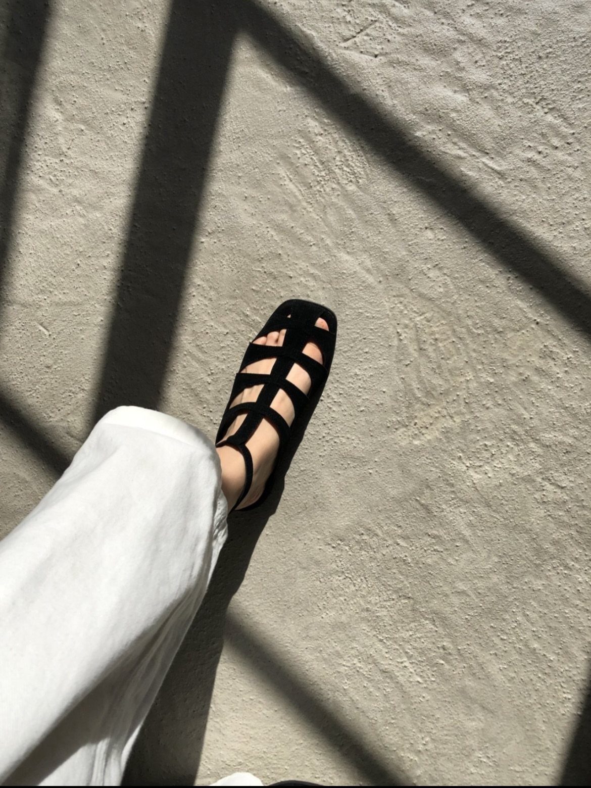Black strappy gladiator sandals worn on a foot against a textured grey concrete background.