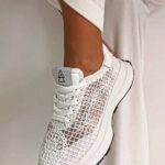 A white lace-patterned sneaker worn on a person's foot against a white background.