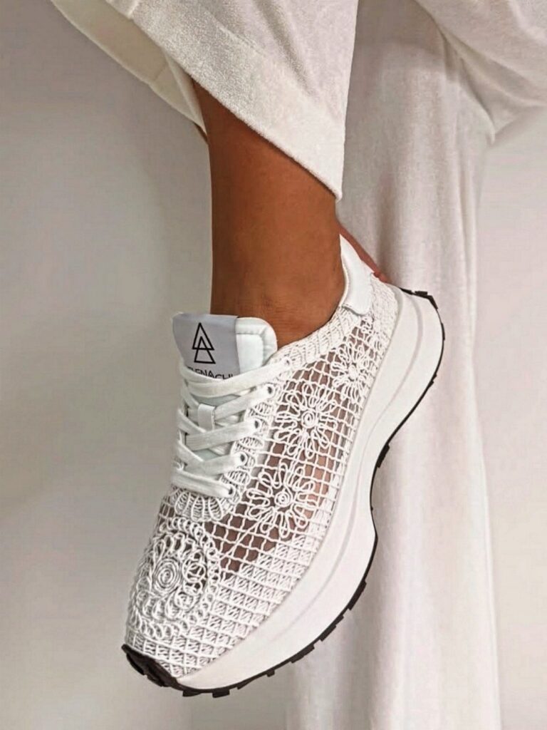 A white lace-patterned sneaker worn on a person's foot against a white background.