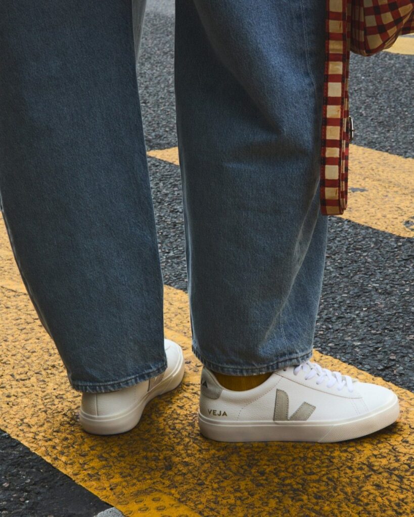 White Veja Campo sneakers worn with blue denim jeans on a street with yellow markings.