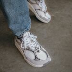 Light grey and white mesh sneakers worn with blue denim jeans on concrete.